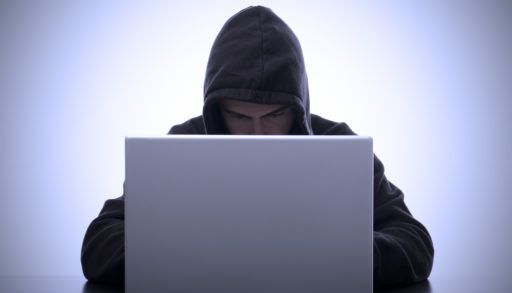 Hacker in a grey hoodie with the hood up on a computer.