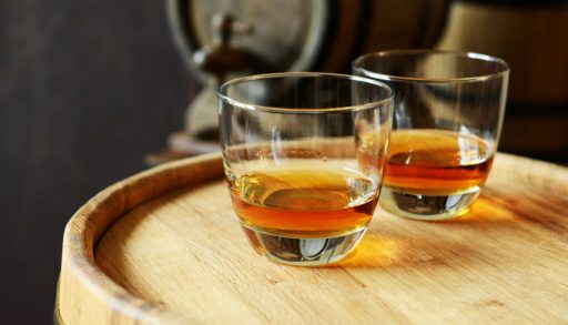 Two glasses of brandy sitting on a wooden barrel.