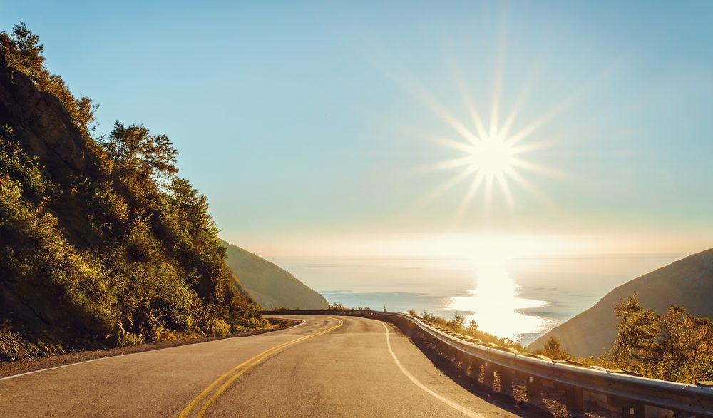 Road bordered by a hill and a cliff that overlooks the ocean in Cape Breton, Nova Scotia, Canada.