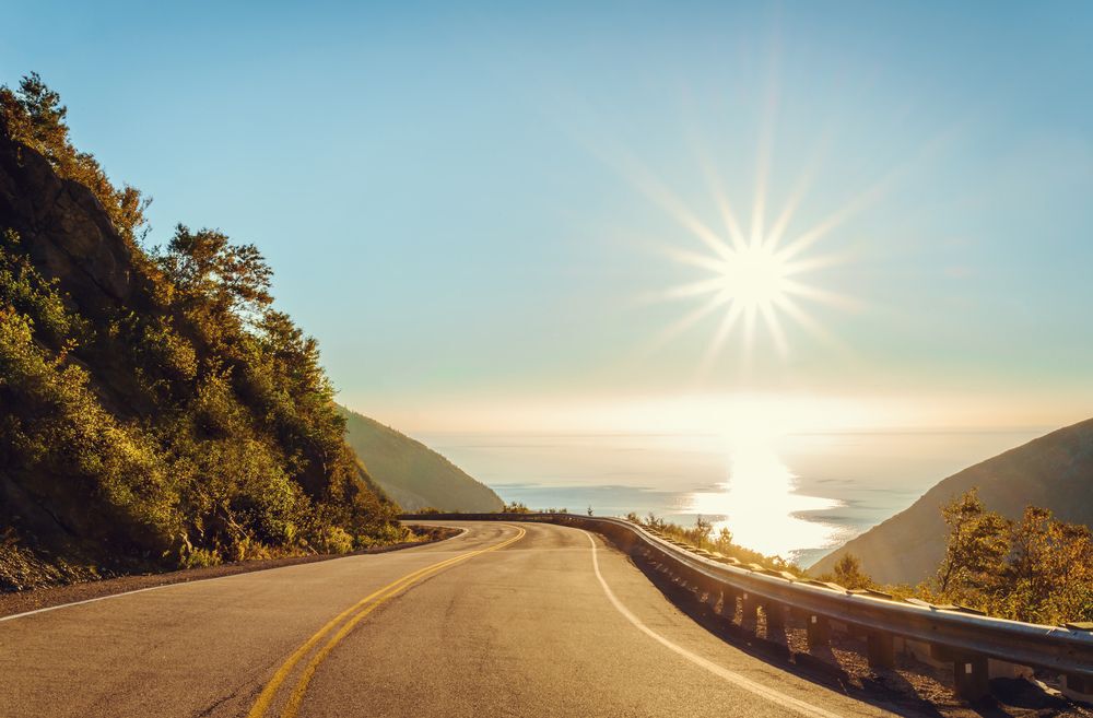 Road bordered by a hill and a cliff that overlooks the ocean in Cape Breton, Nova Scotia, Canada.