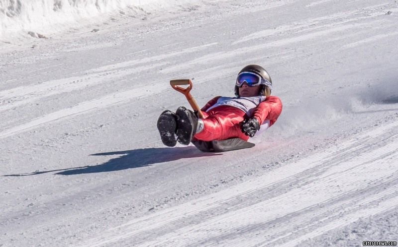 Person in spandex riding a shovel down a snowy hill
