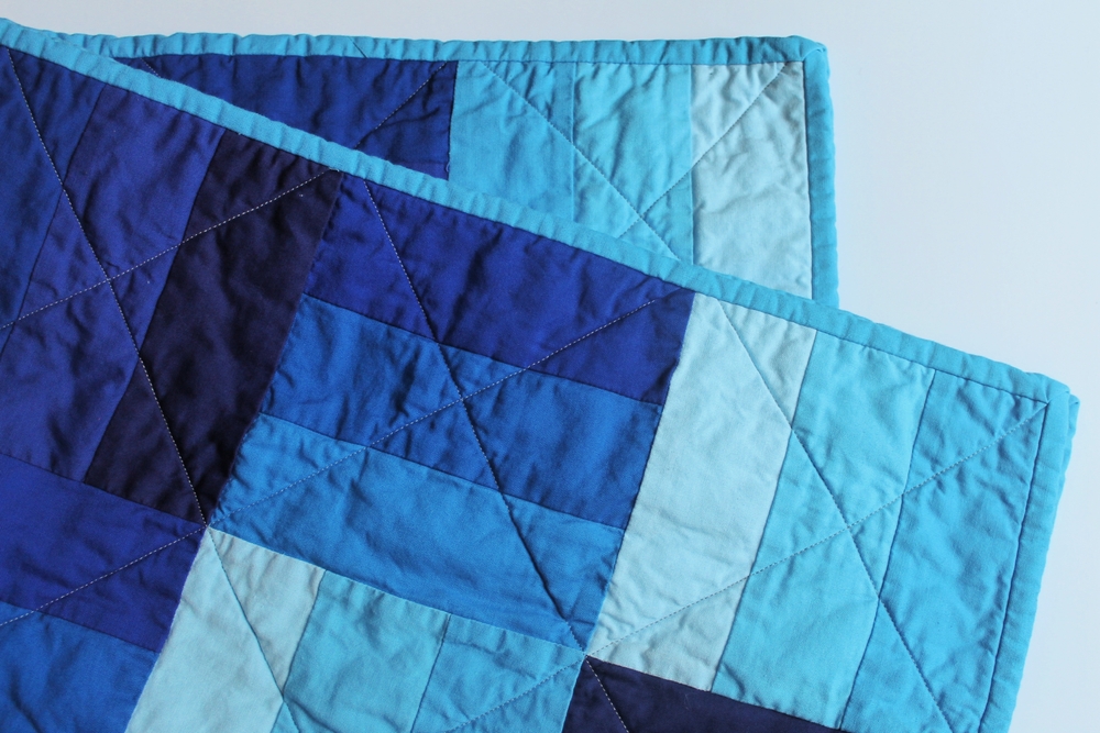 A folded quilt coloured varying shades of blue.