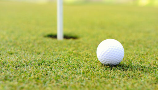 White golf ball approaching hole on a golf green.