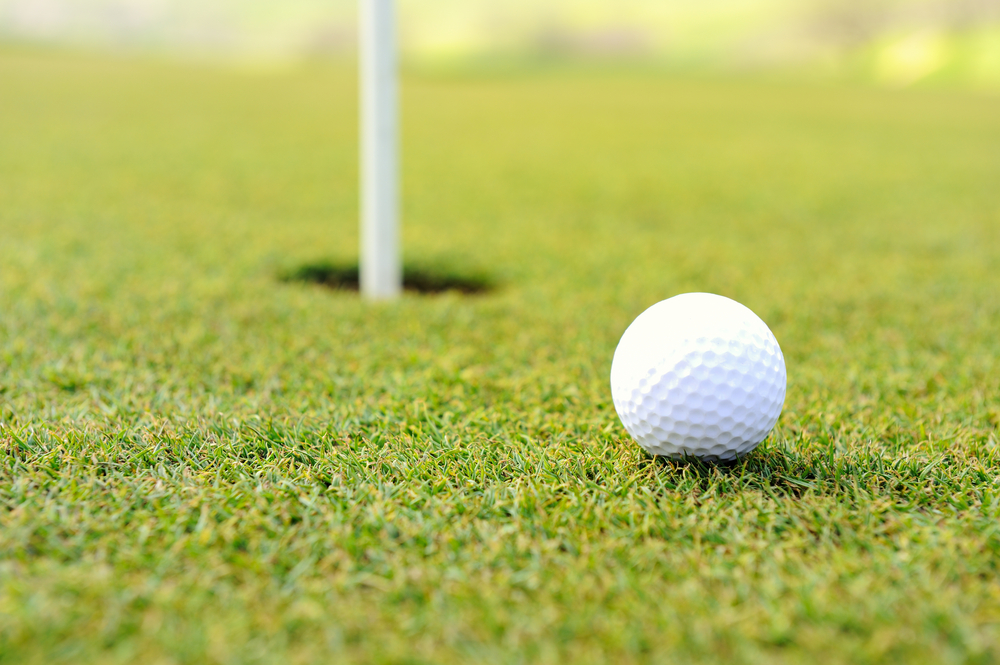 White golf ball approaching hole on a golf green.