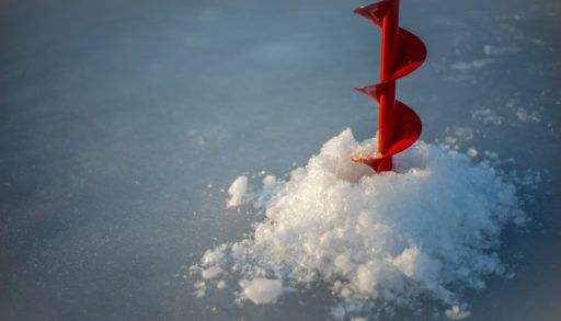 Red ice auger drilling through ice.