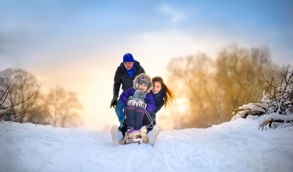 Family tobogganing down a snowy hill at sunset.