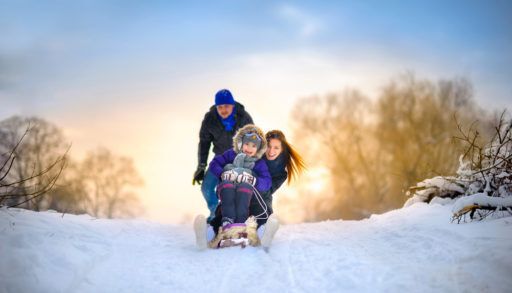 Family tobogganing down a snowy hill at sunset.