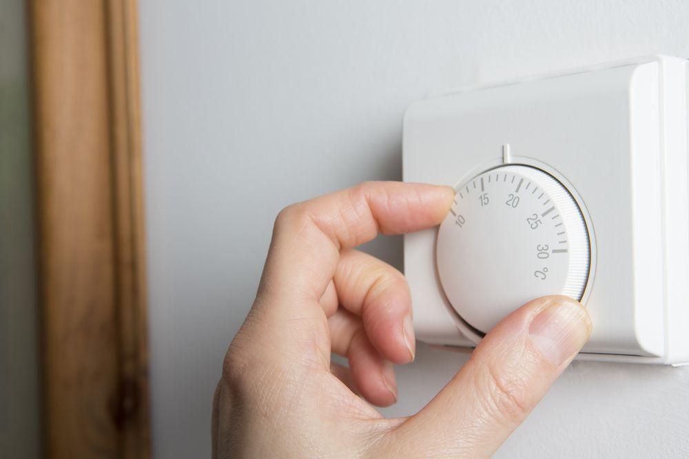 Person adjusting a white thermostat on the wall.