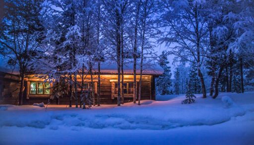 Lit up cozy winter cabin in the woods at dusk.