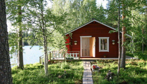 Small wooden red cabin by a lake in the woods.