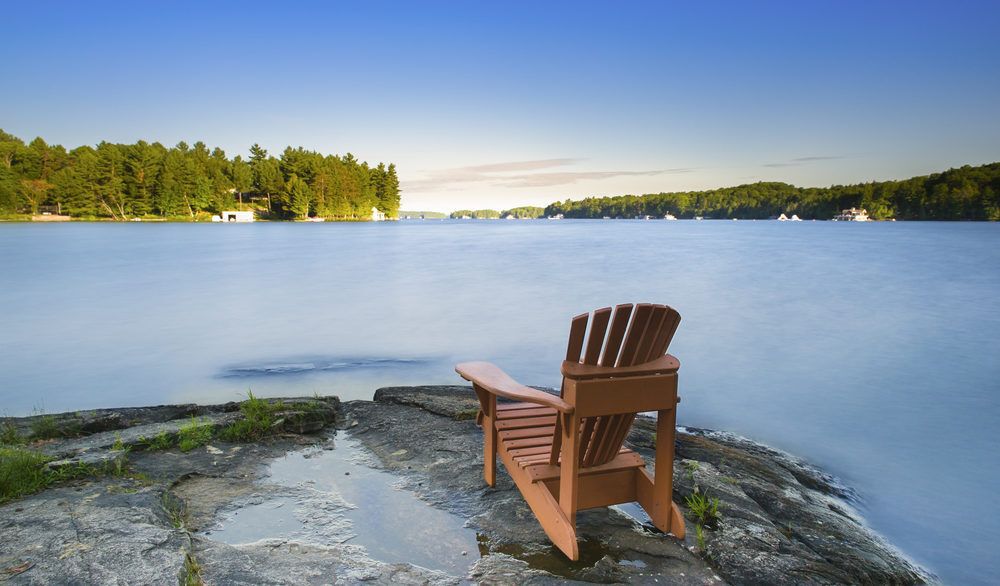 Adirondack chair on a rock by a lake in cottage country.