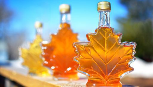 Three maple leaf shaped maple syrup bottles filled with varying shades of maple syrup on an outdoor railing.