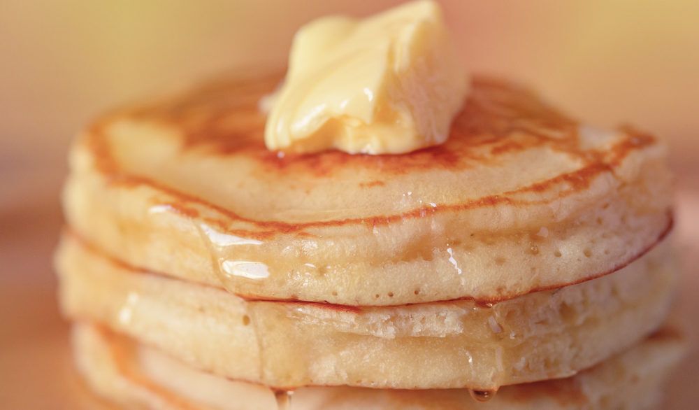 Close-up of a stack of pancakes with maple syrup and butter on top.