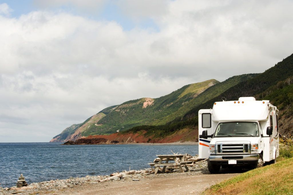 White RV trailer parked at a picnic area by the ocean in Cape Breton, Nova Scotia, Canada.