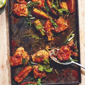 Black rectangular pan with chicken in a red sauce and greens mixed in with it.
