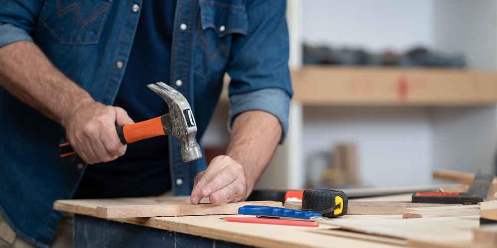 Man hammering a nail into a piece of wood in a workshop.
