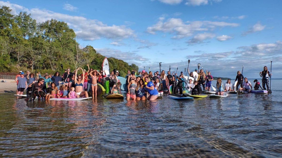 Large group of women posed for group photo with boards in the lake