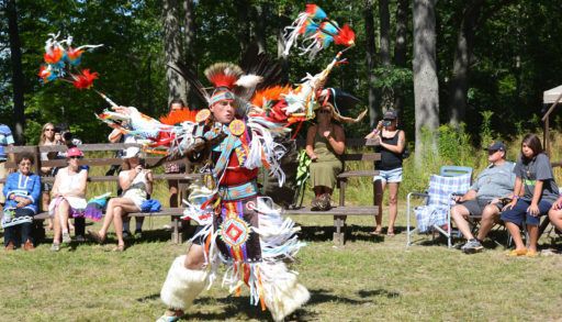 A man in pow wow regalia dances outside