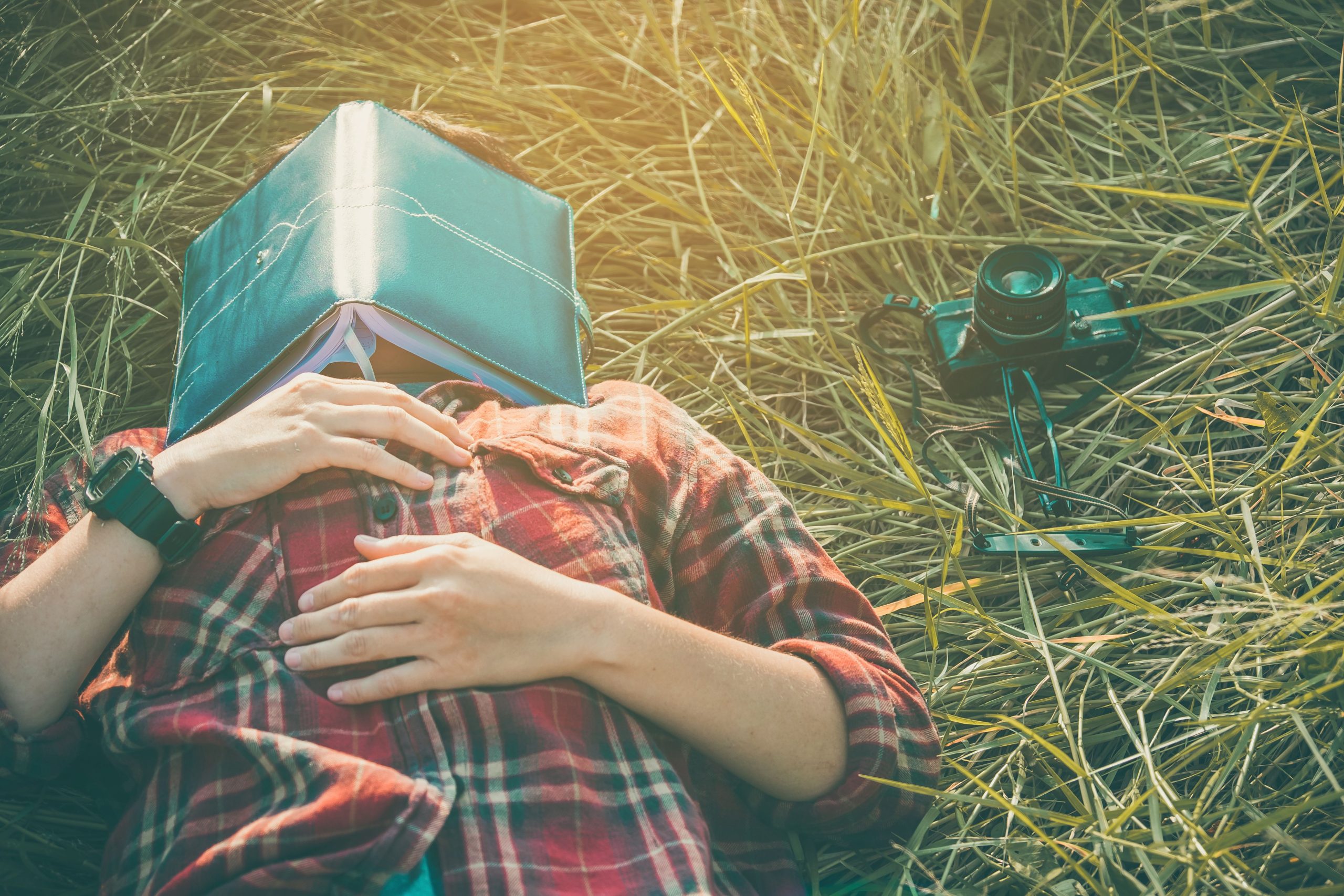 Person sleeping in field with book on face
