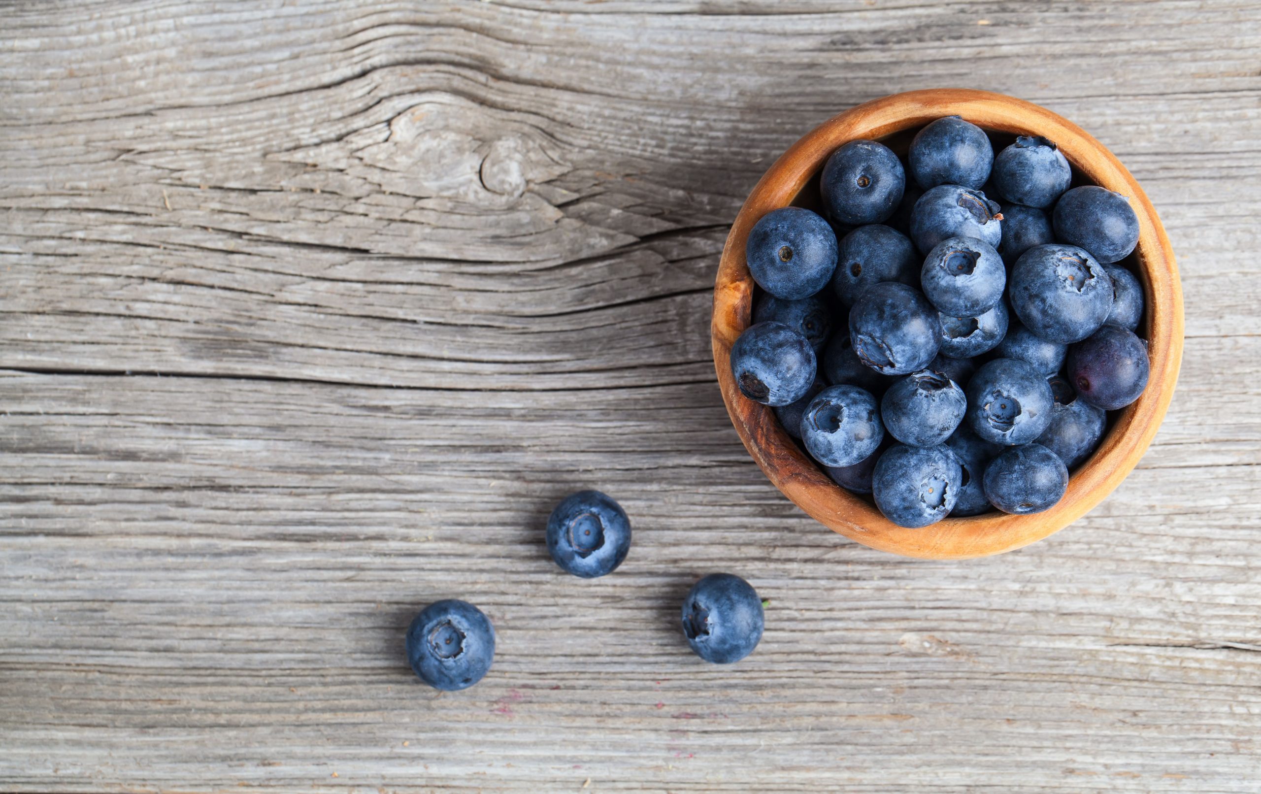 A bowl of blueberries on a wooden table, seen from above
