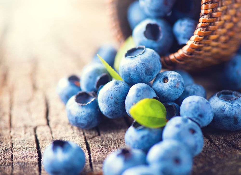 A basket of blueberries spills onto a wooden table