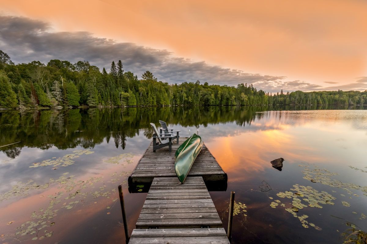Looking down a dock with a green canoe on a lake at sunset.