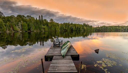 Looking down a dock with a green canoe on a lake at sunset.