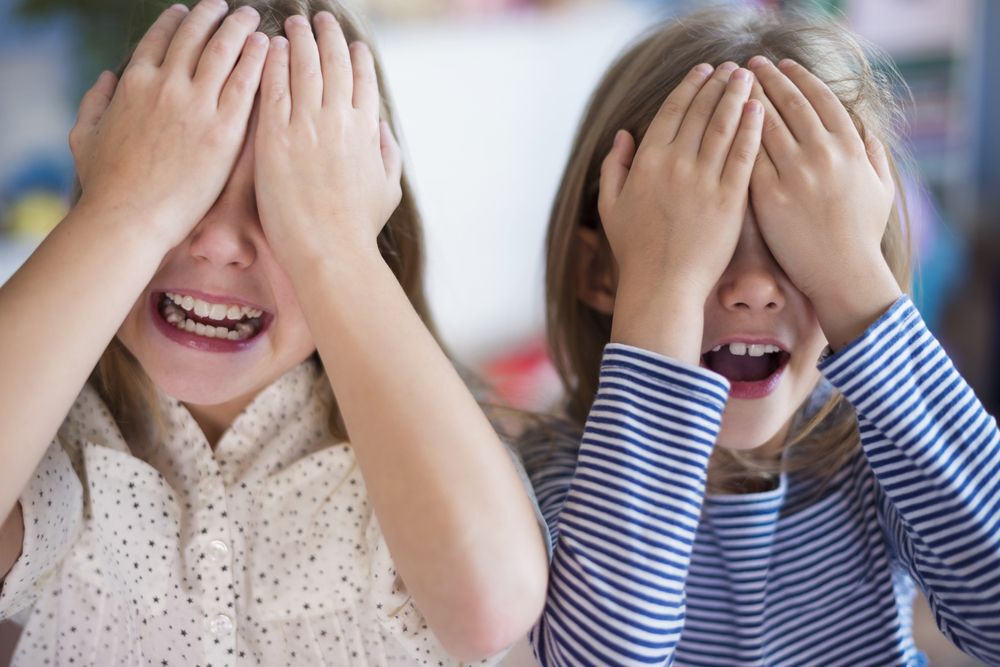 Two little girls cover their eyes with their hands