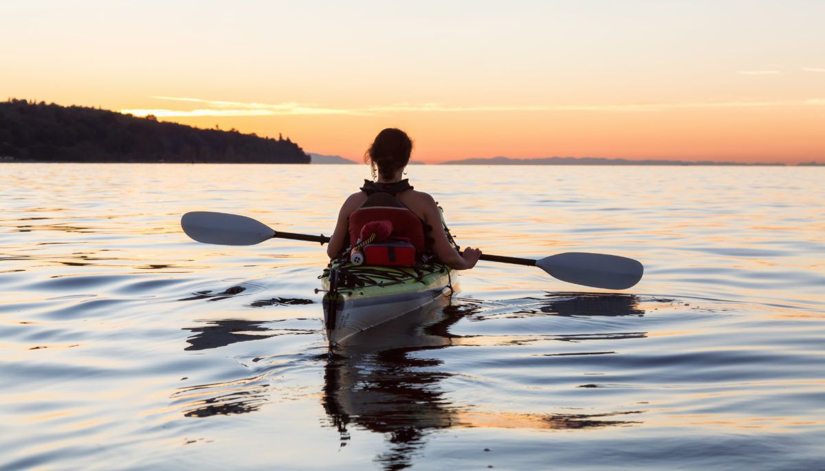 Girl paddling in a kayak on a lake at sunset.
