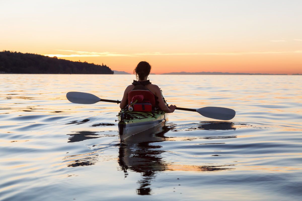 Girl paddling in a kayak on a lake at sunset.