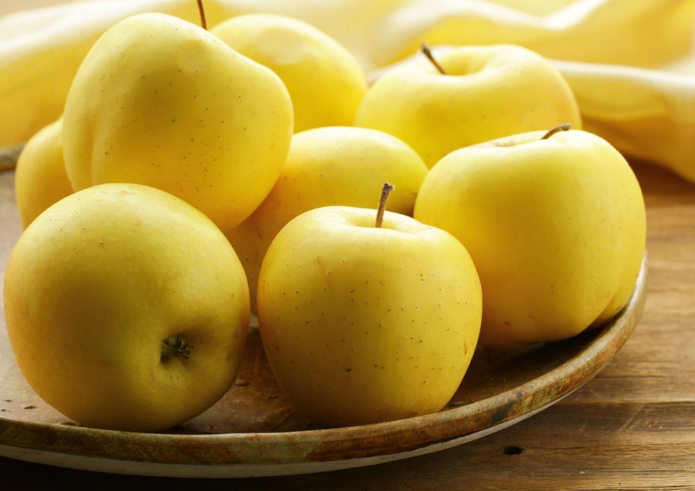Yellow apples sit on a wooden plate