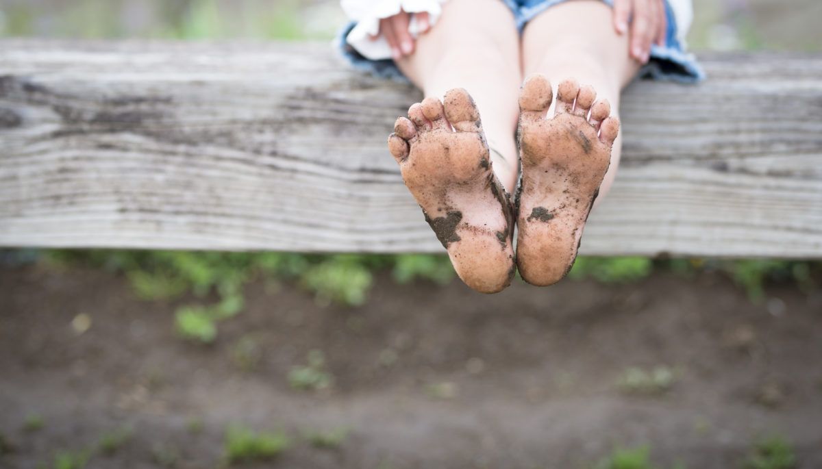 A-child-with-dirty-feet-sits-on-a-fence