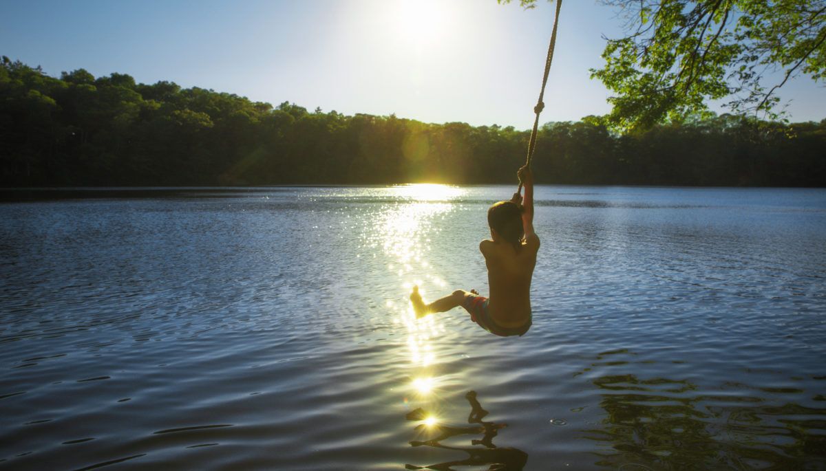 boy-swinging-on-rope-swing-over-lake