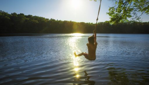 boy-swinging-on-rope-swing-over-lake