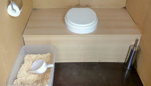 Unusual, unoccupied, recycling composting public toilet, with wood shavings, fully fitted with all mod cons.. scoop, paper, seat and brush.