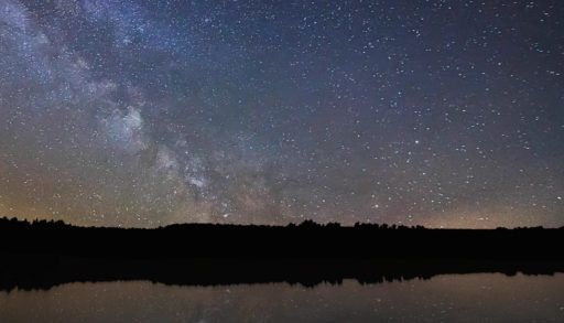 a starry sky in the country with a lake and trees