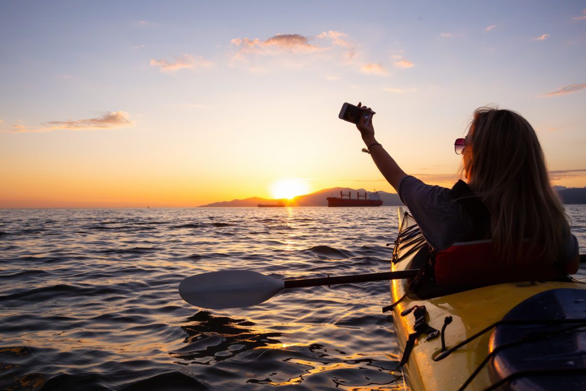 woman-taking-selfie-in-a-kayak-on-lake-at-sunset
