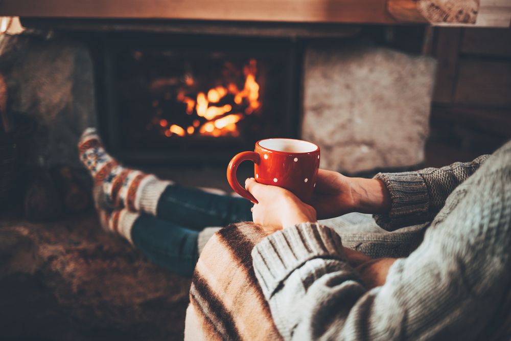 A person sits in front of a fireplace holding a red mug