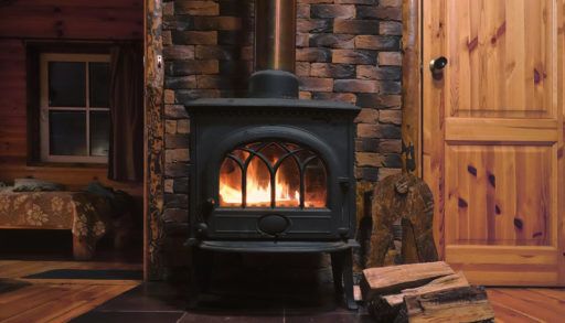 A woodstove with a fire going and firewood alongside