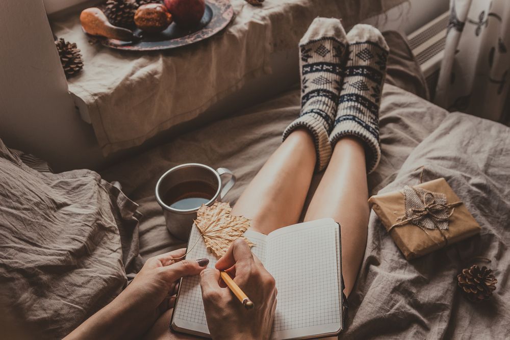 A woman wears woolen socks as she sits with a mug of tea, a book and a cookie