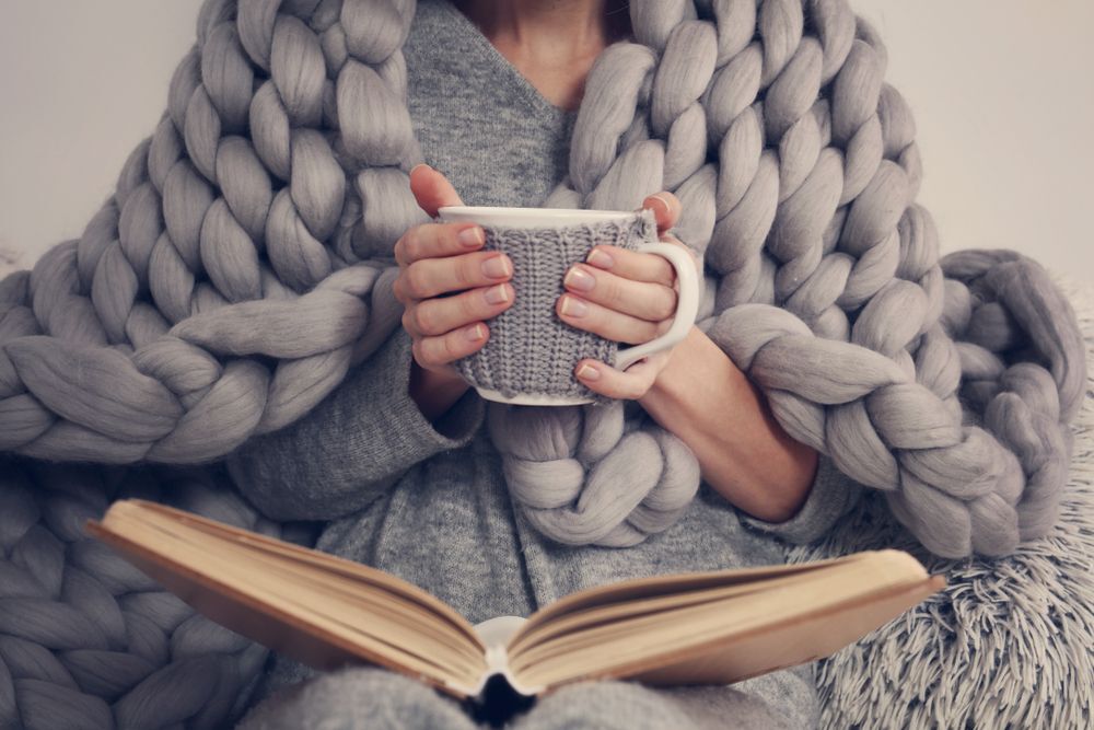 A woman wrapped in a blanket holds a mug