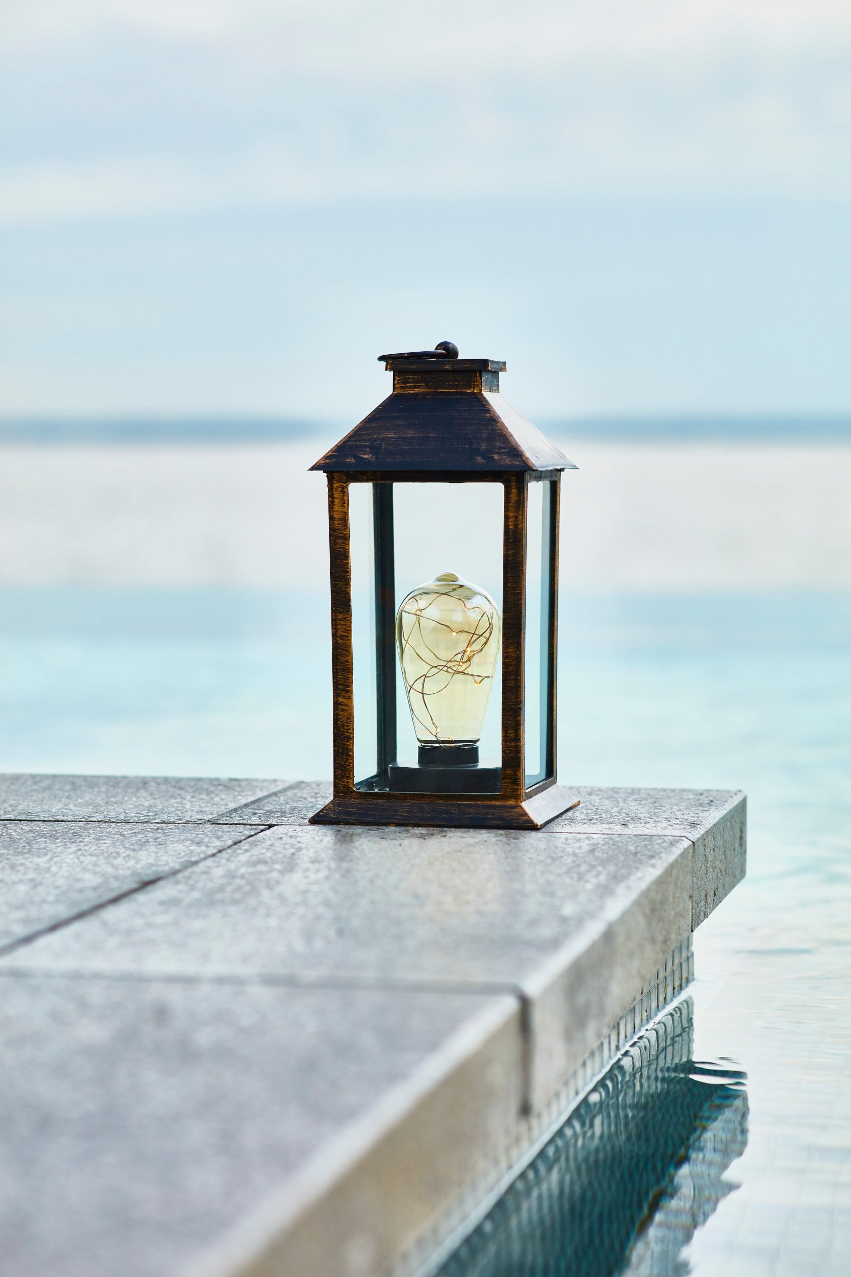 A lantern on a patio table by the water.