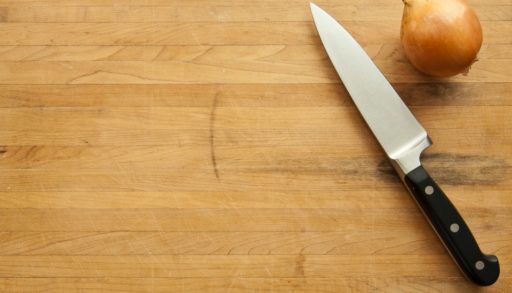 A view looking down on a large knife and onion on a worn butcher block cutting board