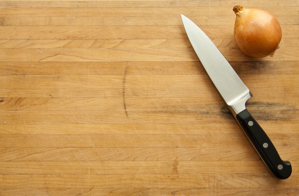 A view looking down on a large knife and onion on a worn butcher block cutting board