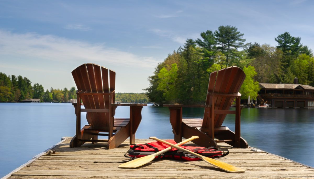 two-adirondack-chairs-on-a-wooden-dock-with-canoe-paddles