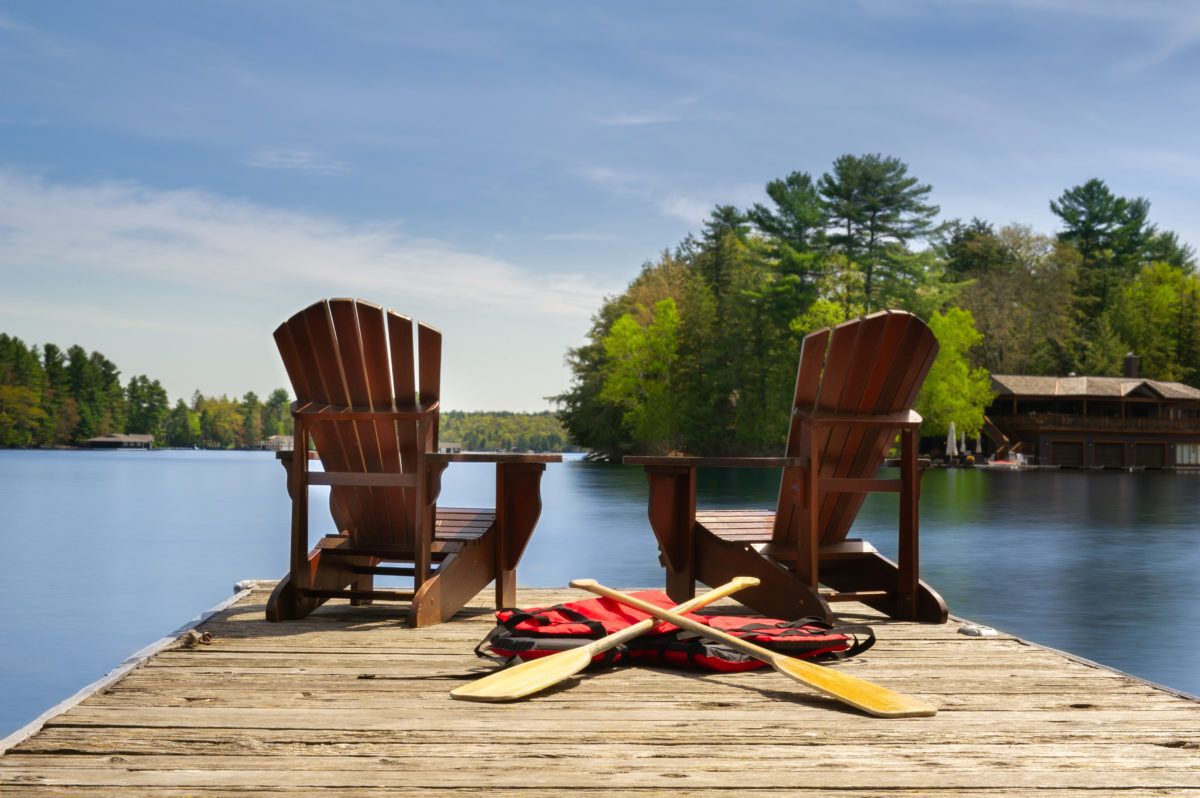 two-adirondack-chairs-on-a-wooden-dock-with-canoe-paddles