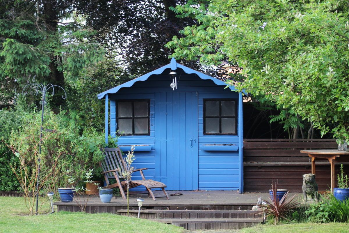 blue-shed-surrounded-by-trees-with-a-chair-in-front