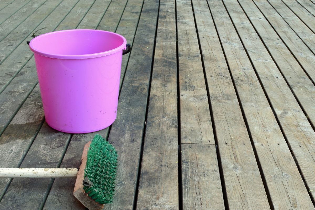 A pink bucket and a scrub brush on a dirty wooden deck.