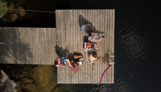 Top down aerial drone image of people sitting on a wooden dock at a cottage lake.