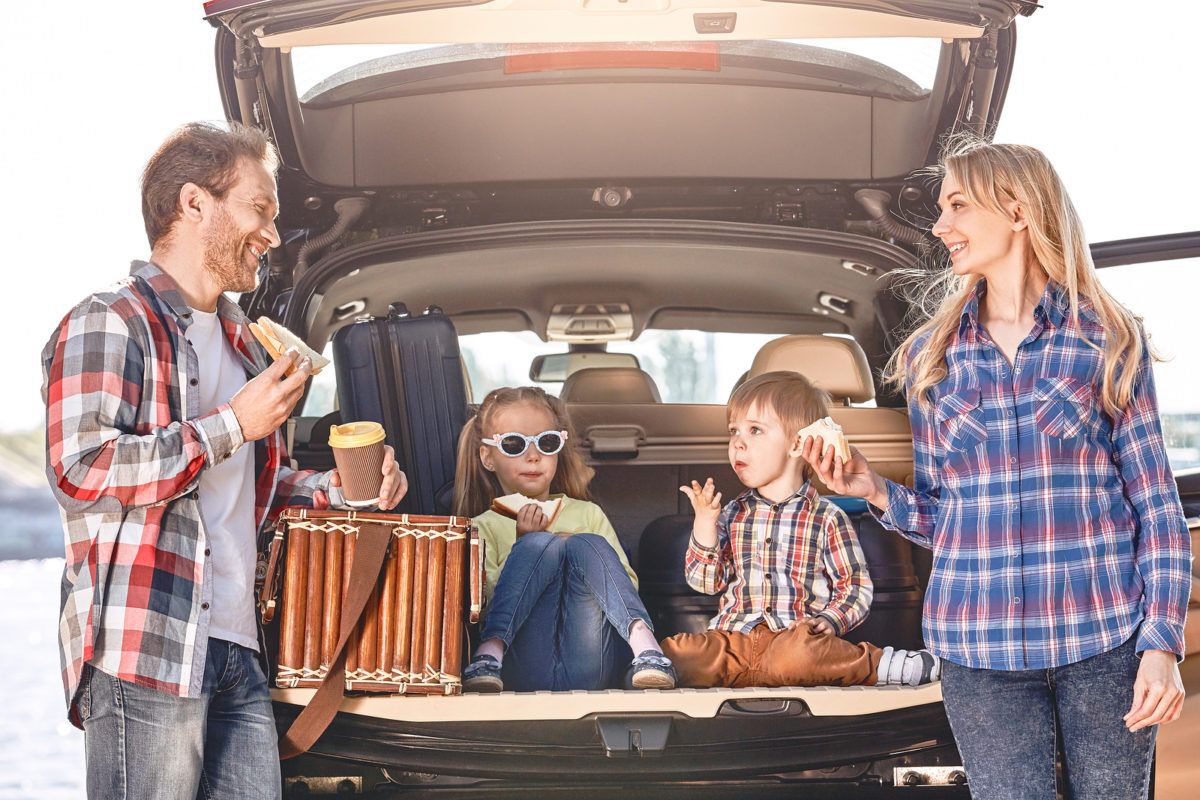 Family of four on a road-trip eating lunch together at the rear of their SUV